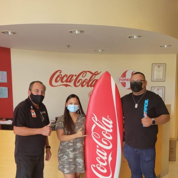 Coca-Cola Beverage Co. (Guam), Inc. Sales Manager Jose 
Fernandez (left) and Business Consultant Robby Yamasta (right), 
award a Coca-Cola Surfboard to Marie A. Manglona at the “Chill 
with Coke” holiday promo prize presentation held at the CocaCola corporate offices in Barrigada Heights in February 2021.
